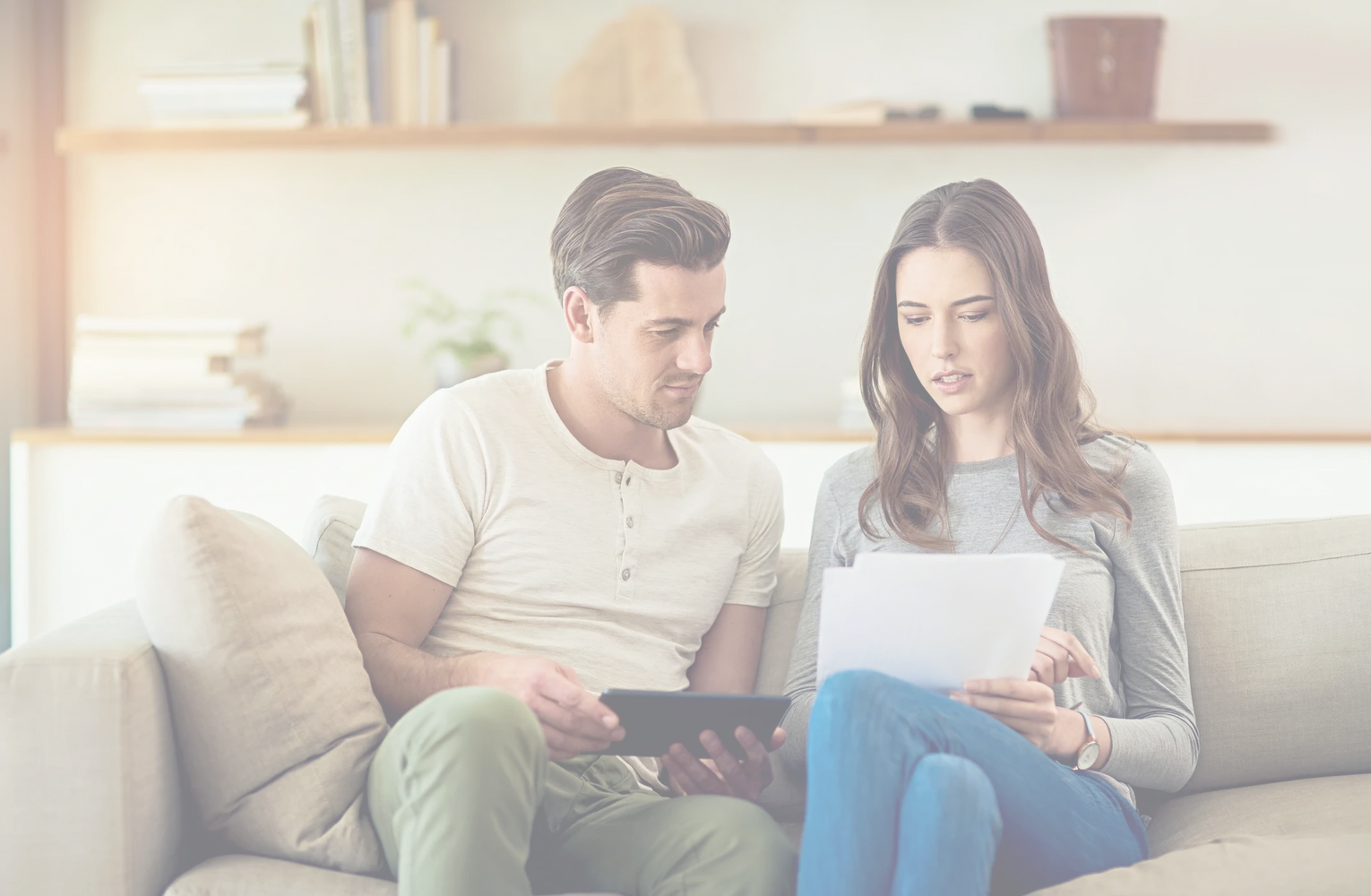 Couple sitting on a couch reviewing documents and a tablet together.