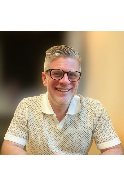 Smiling man with glasses wearing a patterned polo shirt.