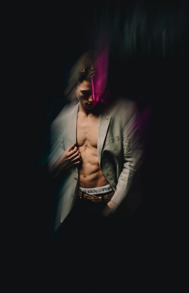 Male model in sports coat, no shirt in moody dark portrait.