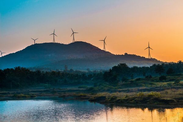 Wind turbines on a hill during sunset over a calm water body.
