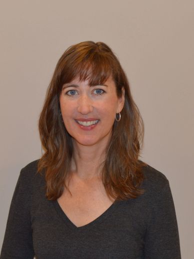 Smiling woman with brown hair and blue eyes wearing a dark gray top.