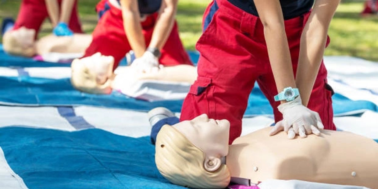 People practicing CPR on mannequins outdoors during a training session.