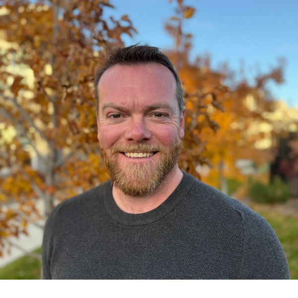 Smiling man with a beard wearing a gray zip-up sweater outdoors.