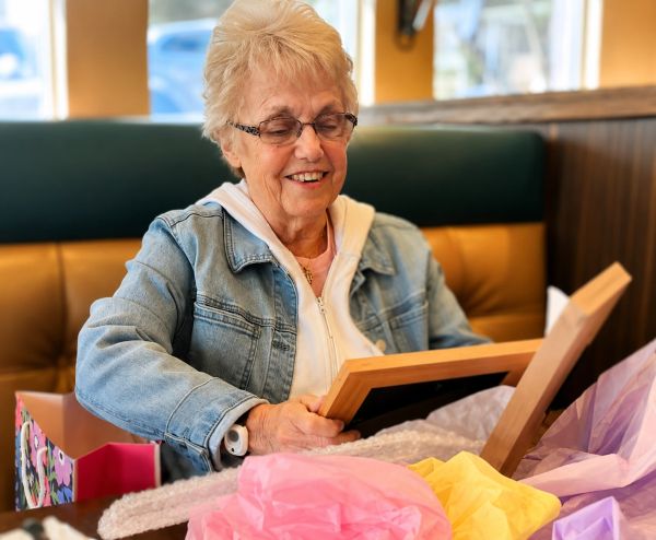 Elderly woman happily opening a framed gift.