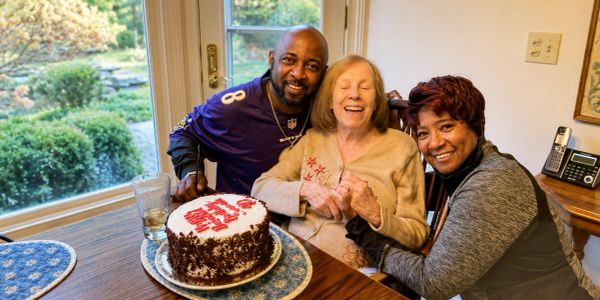 Three people celebrate with a cake at a table.