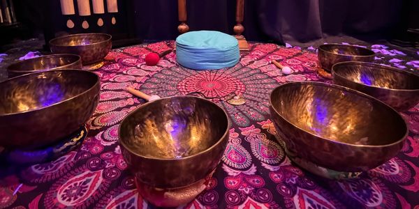 Meditative setup with singing bowls, mallets, and floral book artwork on a patterned cloth.