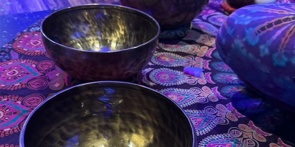 Four brass singing bowls on a colorful patterned cloth with a mallet nearby.