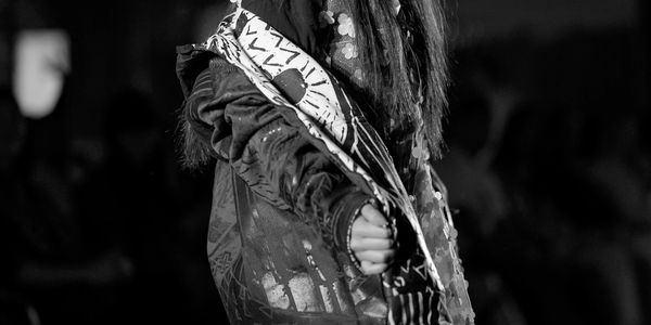 Black and white photo of a person wearing an artistic jacket with a patterned scarf.