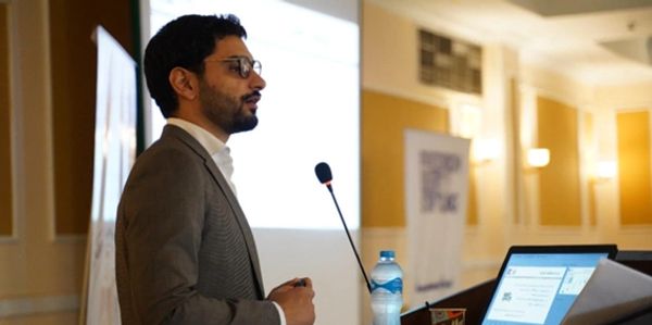 Man in glasses giving a presentation with a laptop and microphone.