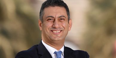 Confident man in a suit smiling outdoors with blurred background.
