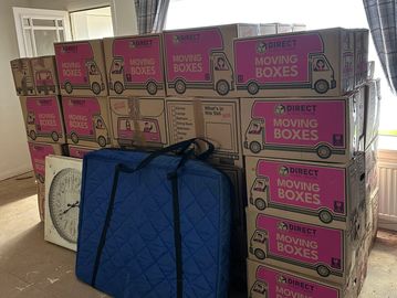 Stack of moving boxes and a blue padded bag in a room.