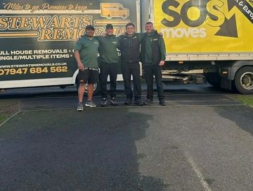 Four men standing in front of yellow moving trucks.