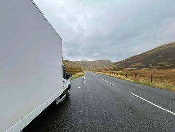 White truck on a winding road in a hilly landscape.