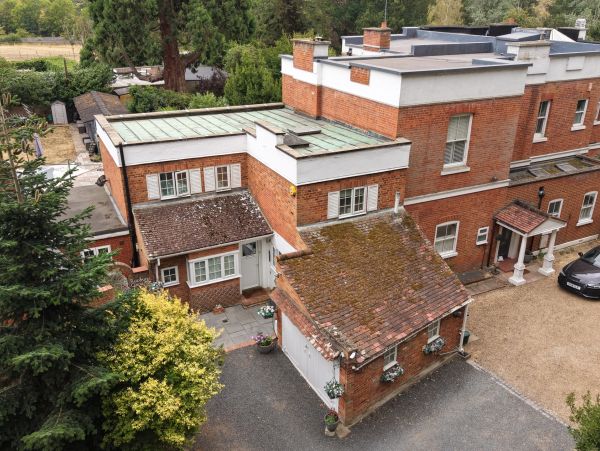 Large brick house with multiple roofs and surrounded by greenery.