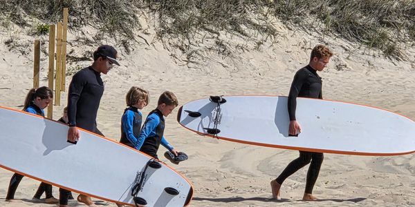 People carrying surfboards on a sandy beach.