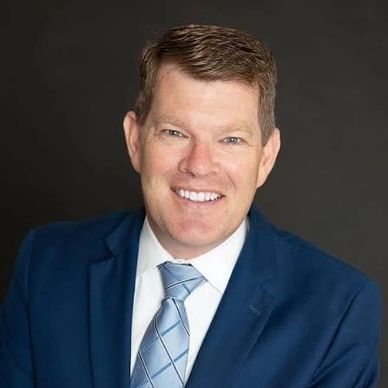 Man smiling in a blue suit and tie.