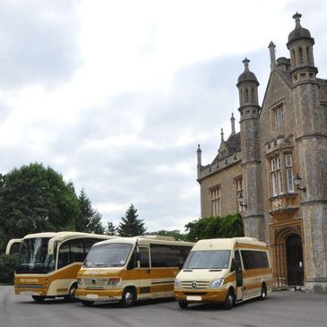 Three yellow and white minibuses parked beside a historic stone building under a cloudy sky.