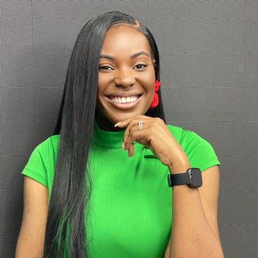 Smiling woman in a green top with long hair and red earrings.