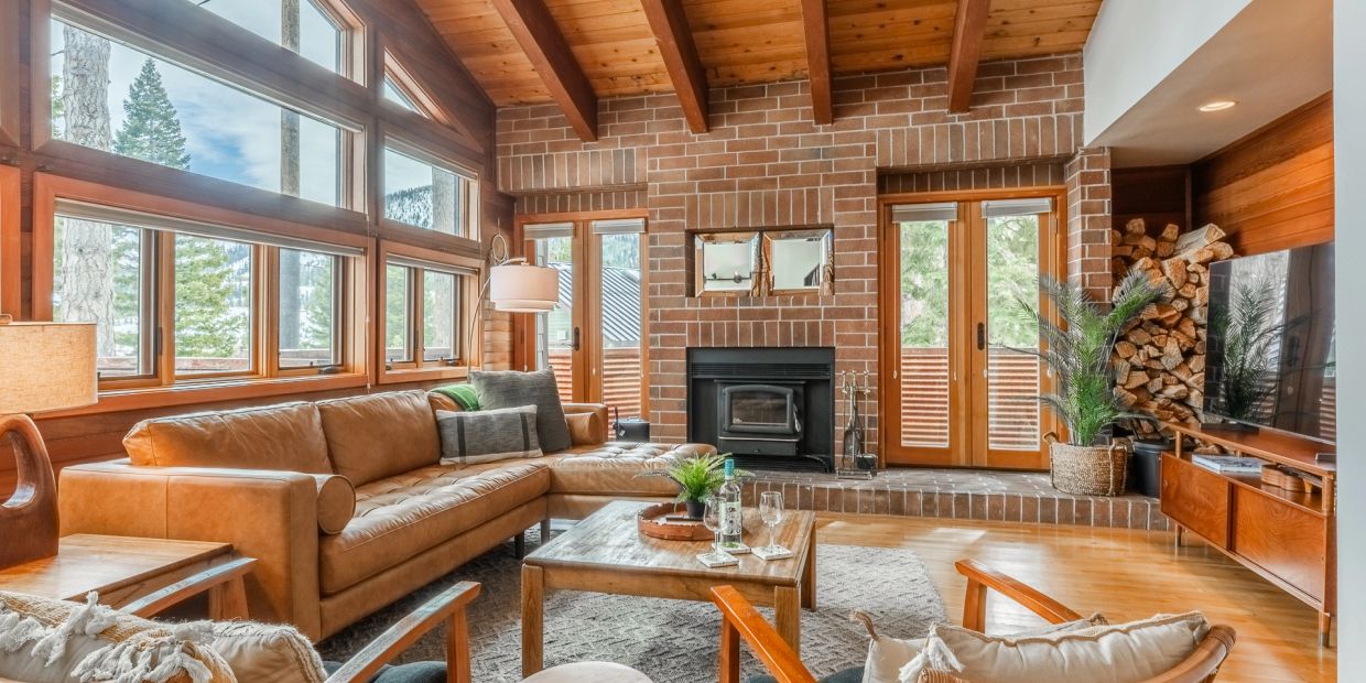 Cozy living room with large windows, leather sofa, fireplace, and wooden accents.