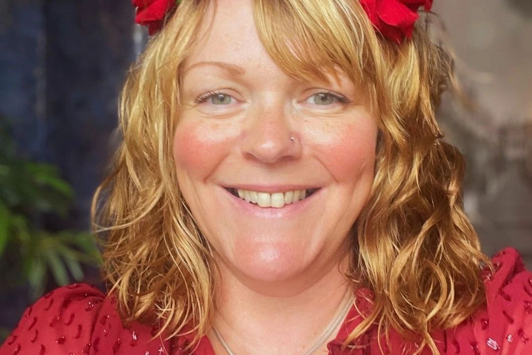 Smiling woman with blonde hair wearing a red top and red hair accessories.
