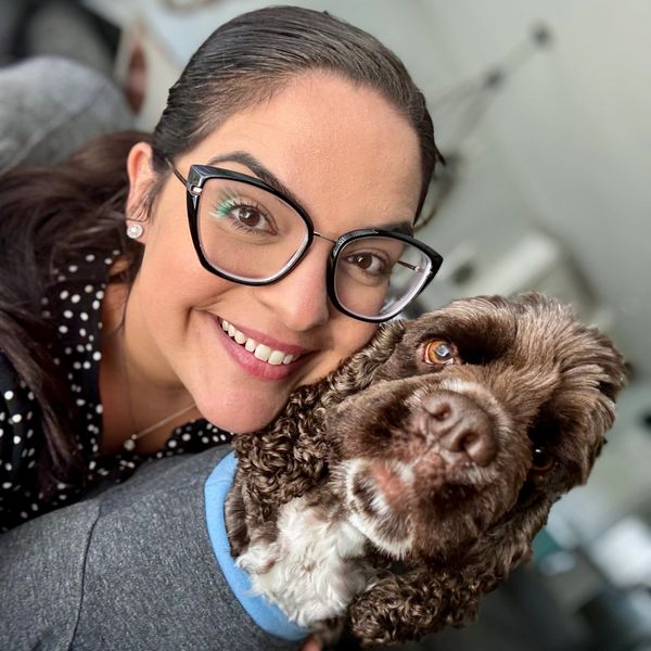 Smiling woman with glasses cuddles her curly-haired dog.