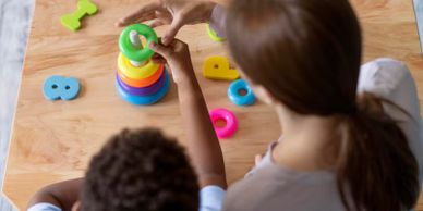 A child and adult playing with a colorful stacking toy.