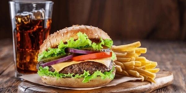 A cheeseburger with lettuce, tomato, onion, fries, and a glass of soda.
