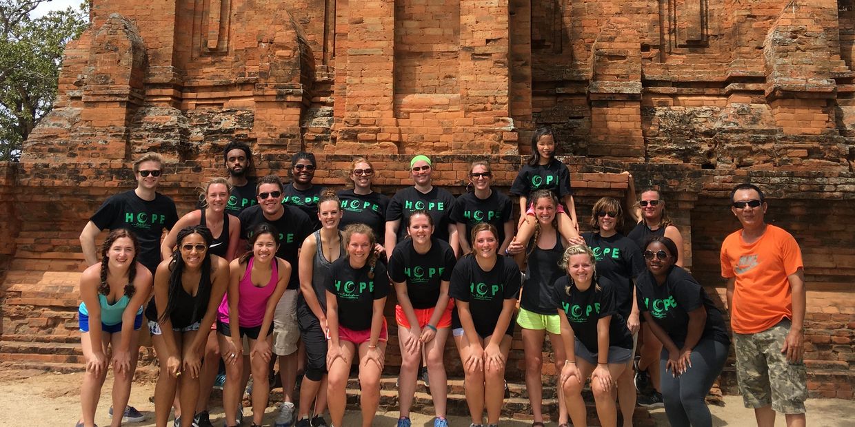 Group photo of diverse young adults and a child in front of an ancient brick structure.