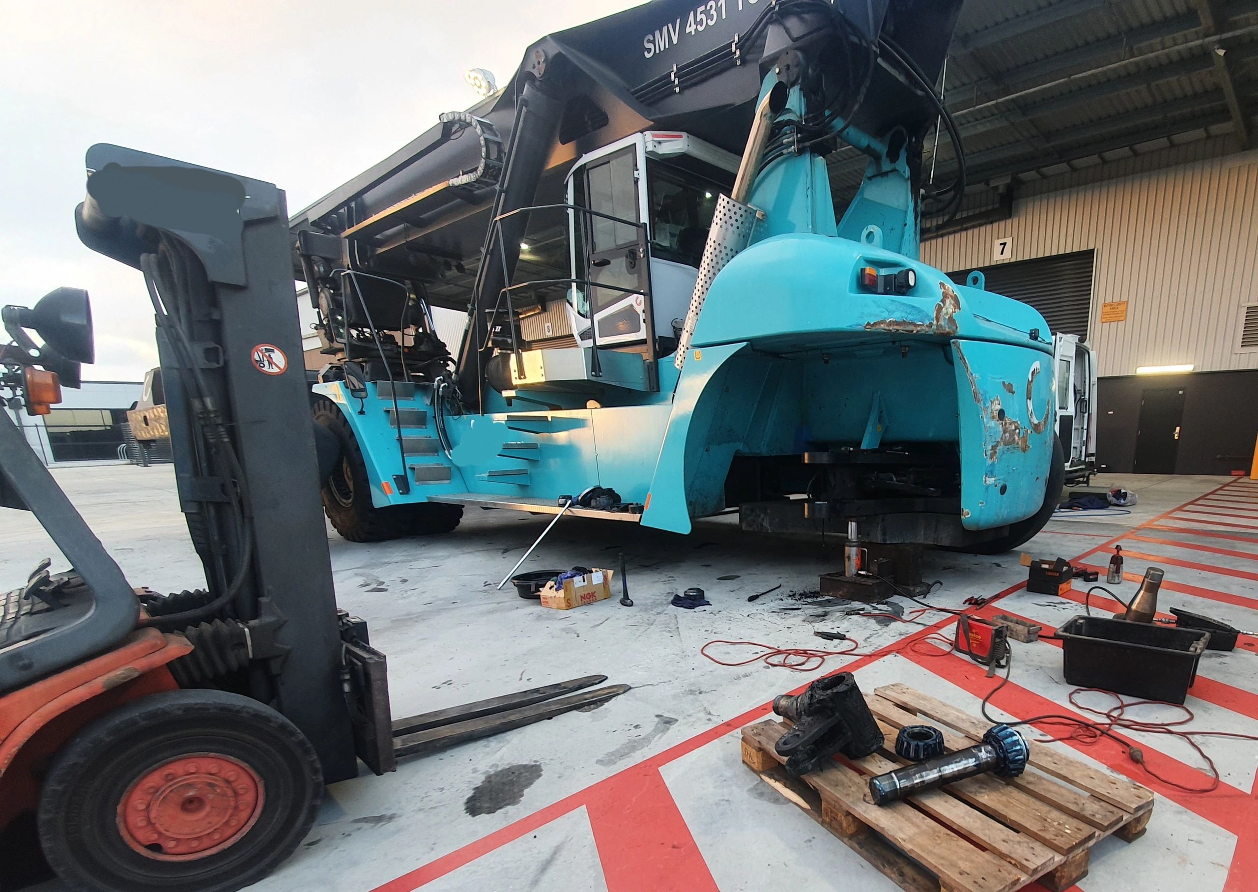 Heavy machinery undergoing maintenance with parts and tools spread out on the floor.