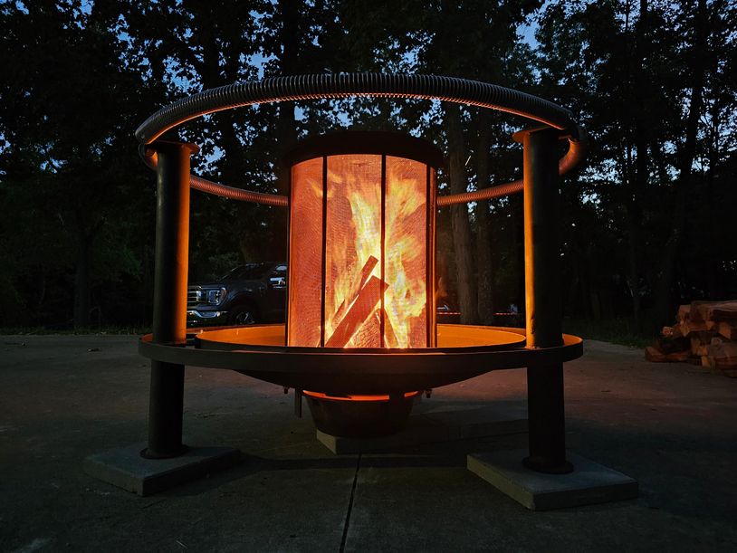 A glowing fire burns inside a modern outdoor fire pit at dusk.