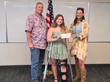 Young woman on crutches receives award check with two adults.