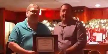 Two men holding a framed certificate in a warmly lit room.