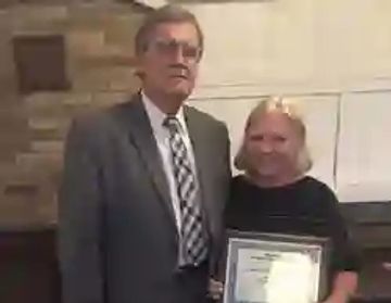 Two people standing together, one holding a framed certificate.