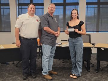 Three people standing with a check being handed over.