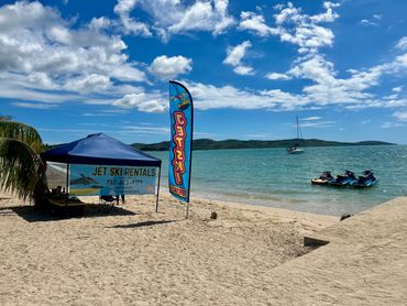 Sunny beach with jet ski rentals and calm ocean waters.
