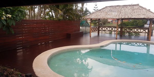 Poolside area with wooden deck and thatched gazebo.