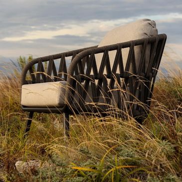 A cushioned outdoor chair in a grassy field under a cloudy sky.