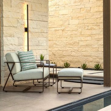 Modern outdoor seating with light cushions and a stone wall backdrop.