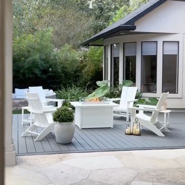 Cozy outdoor patio with white Adirondack chairs and a fire pit on a gray deck.