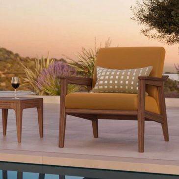 Modern outdoor chair with cushion and side table by the pool at sunset.