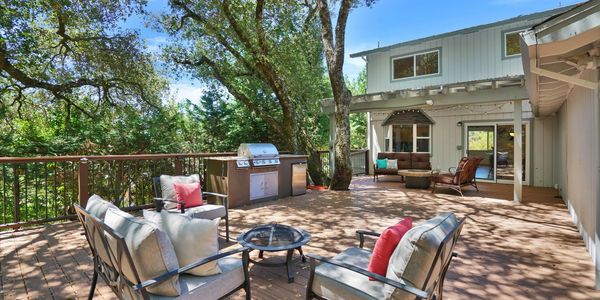 Spacious outdoor patio with seating and grill under trees.
