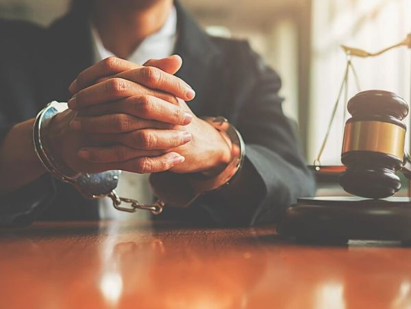 Man in a suit sitting at a desk in handcuffs with a gavel nearby – Criminal defense consultation