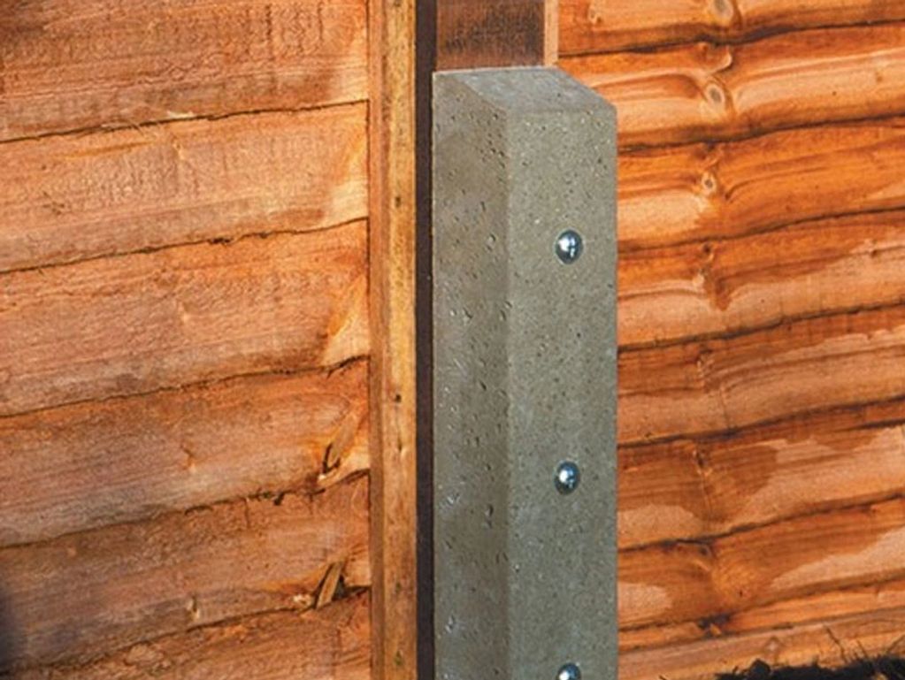 Close-up of a concrete post with bolts attached to a wooden fence.