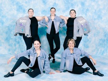 Group of five women in denim jackets posing against a sky backdrop.