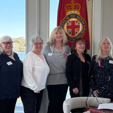 Five women standing together in front of a British flag banner indoors.