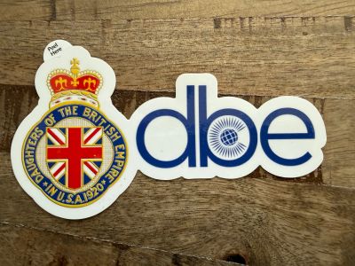 Two stickers on a wooden surface, one with a British emblem and one with the letters 'dbe'.