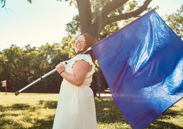 Smiling woman holding a large blue flag outdoors.