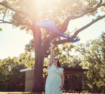 Woman in white dress throwing a scarf outdoors.