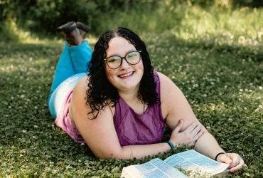 Smiling woman lying on grass with an open book.