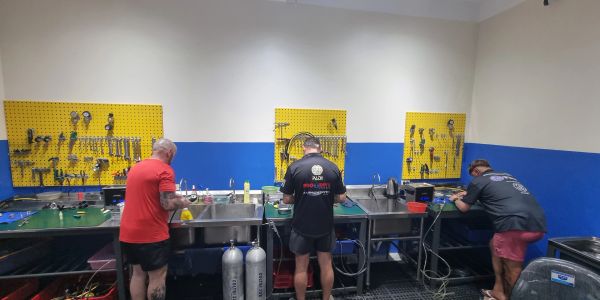 Three men working at tool benches in a workshop.